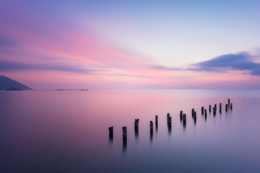 Sunset over a calm body of water with wooden posts sticking out of the water.